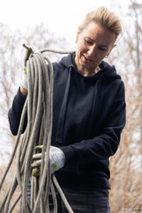 Grafika przedstawia dorosłą kobietę, wolontariuszkę fundacji, zwijającą liny