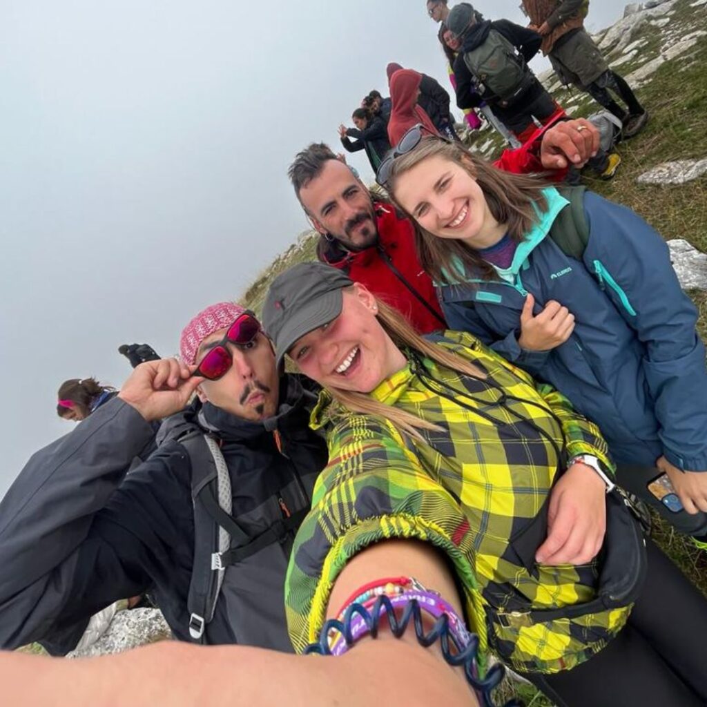 Zdjęcie przedstawia grupę ludzi na wyprawie w wysokich górach, ustawionych z uśmiechem do zdjęcia