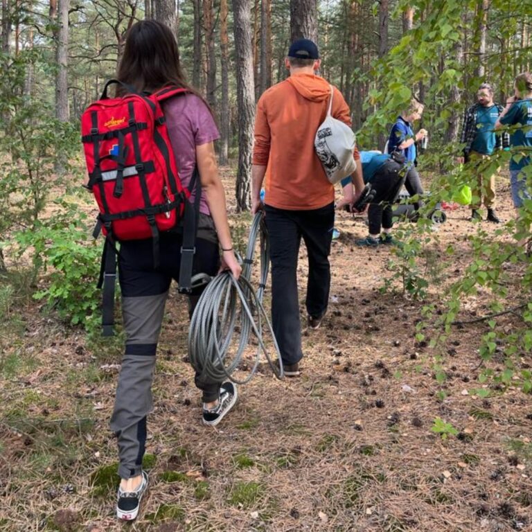Zdjęcie przedstawia grupę przyjaciół wędrujących na wycieczce w lesie w ciągu lata